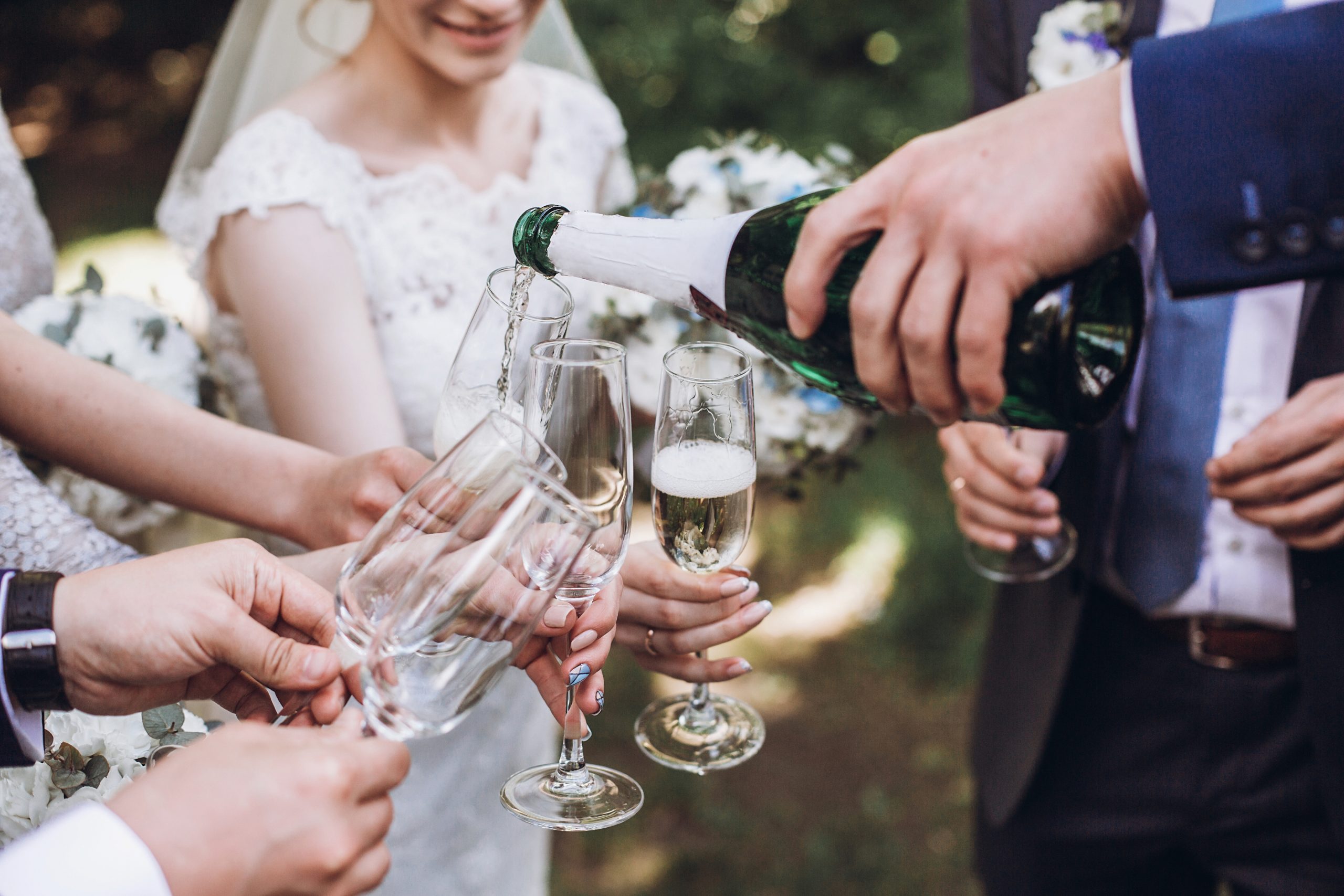 happy group of people toasting with champagne. man holding bottle of champagne and pouring drink into glasses. bride bridesmaids and groom groomsmen having fun. holiday celebration